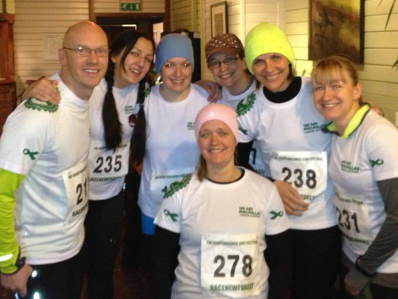 A group of runners smiling for a photo wearing macmillan cancer running tops